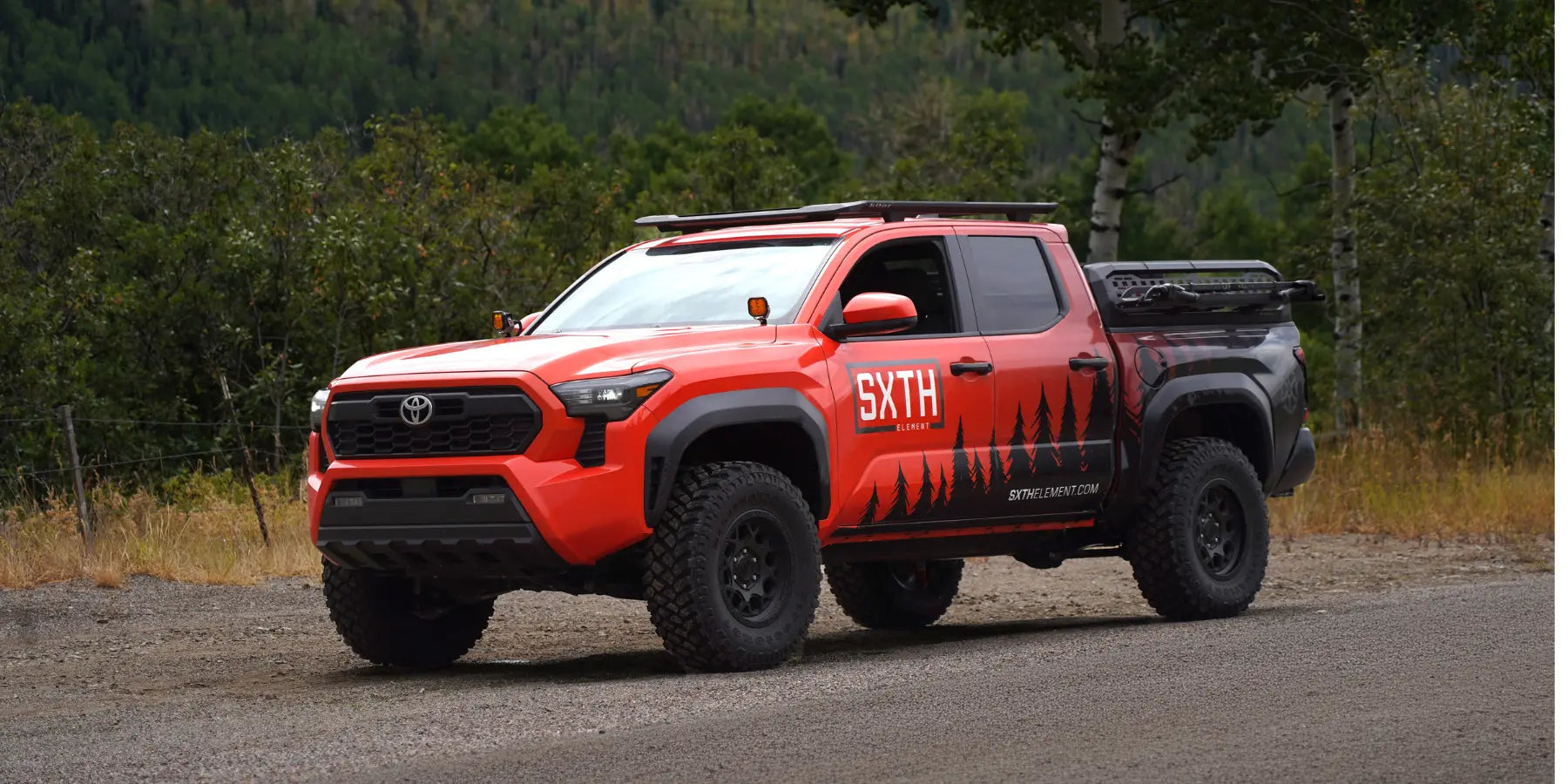 Orange Toyota Tacoma built by SXTH Element with a roof rack and off-road tires